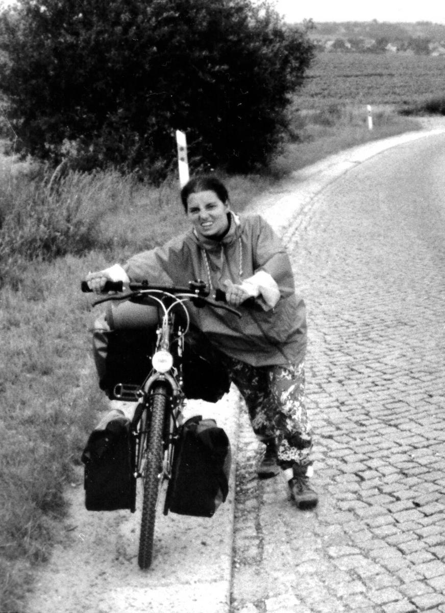 woman walking, pushing a heavy loaded bycicle uphill